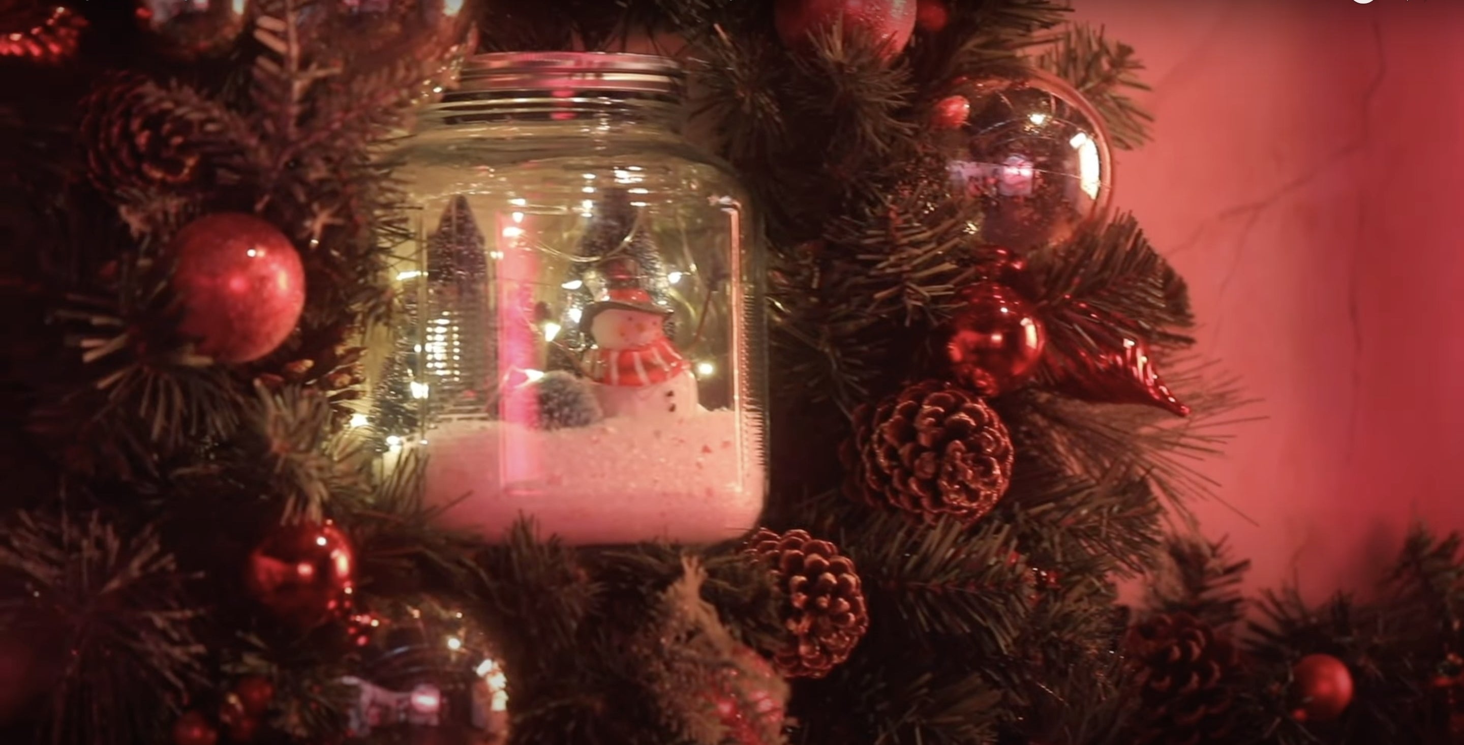 A Mason jar in the middle of a wreath with a Christmas tree and snowman scene