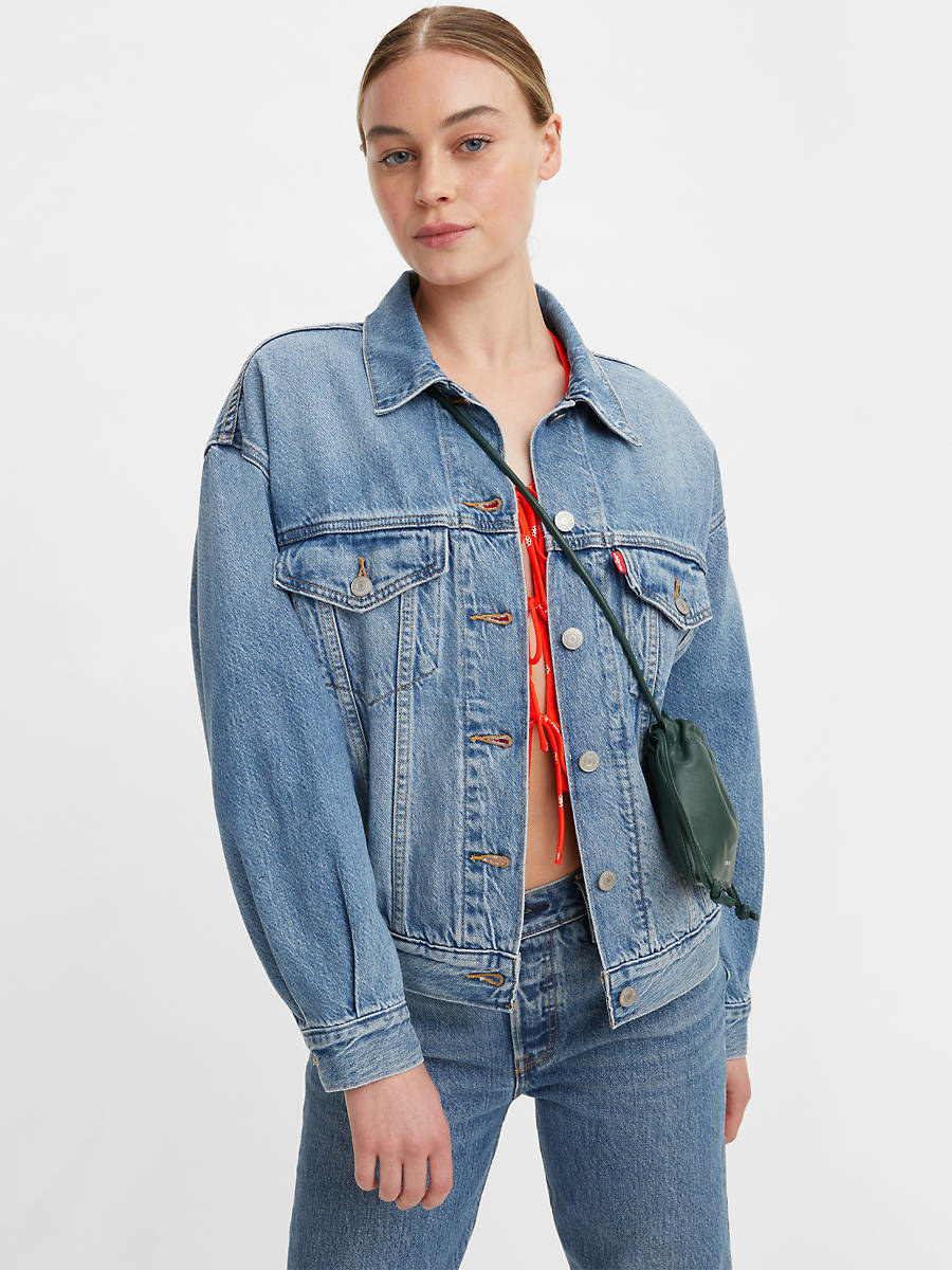 A person wearing a slightly oversized denim jacket in front of a plain background