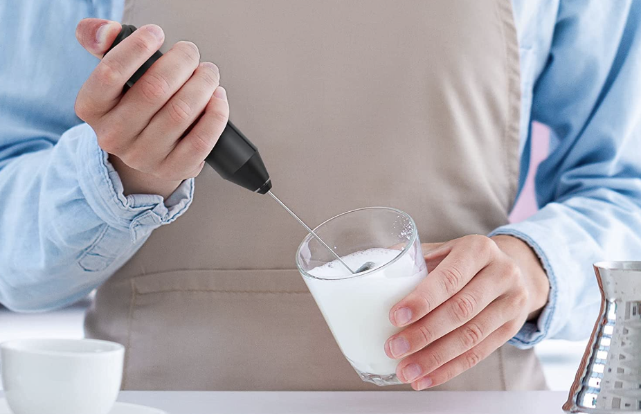 model holding black handheld milk frother to whip up cup of milk