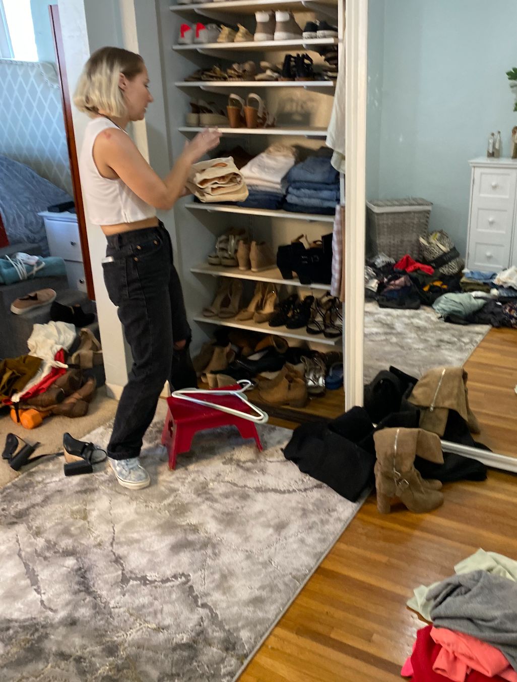 Woman standing in front of shelves with shoes and clothes and putting folded clothes on them