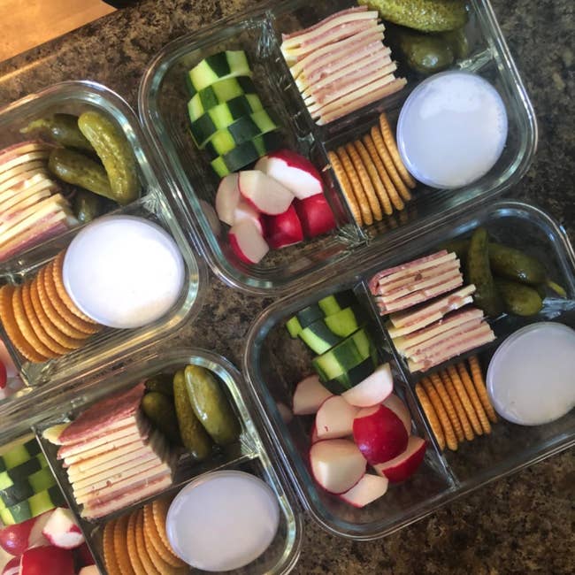 a reviewer shows four containers filled with  veggies, fruit, and crackers in each section.
