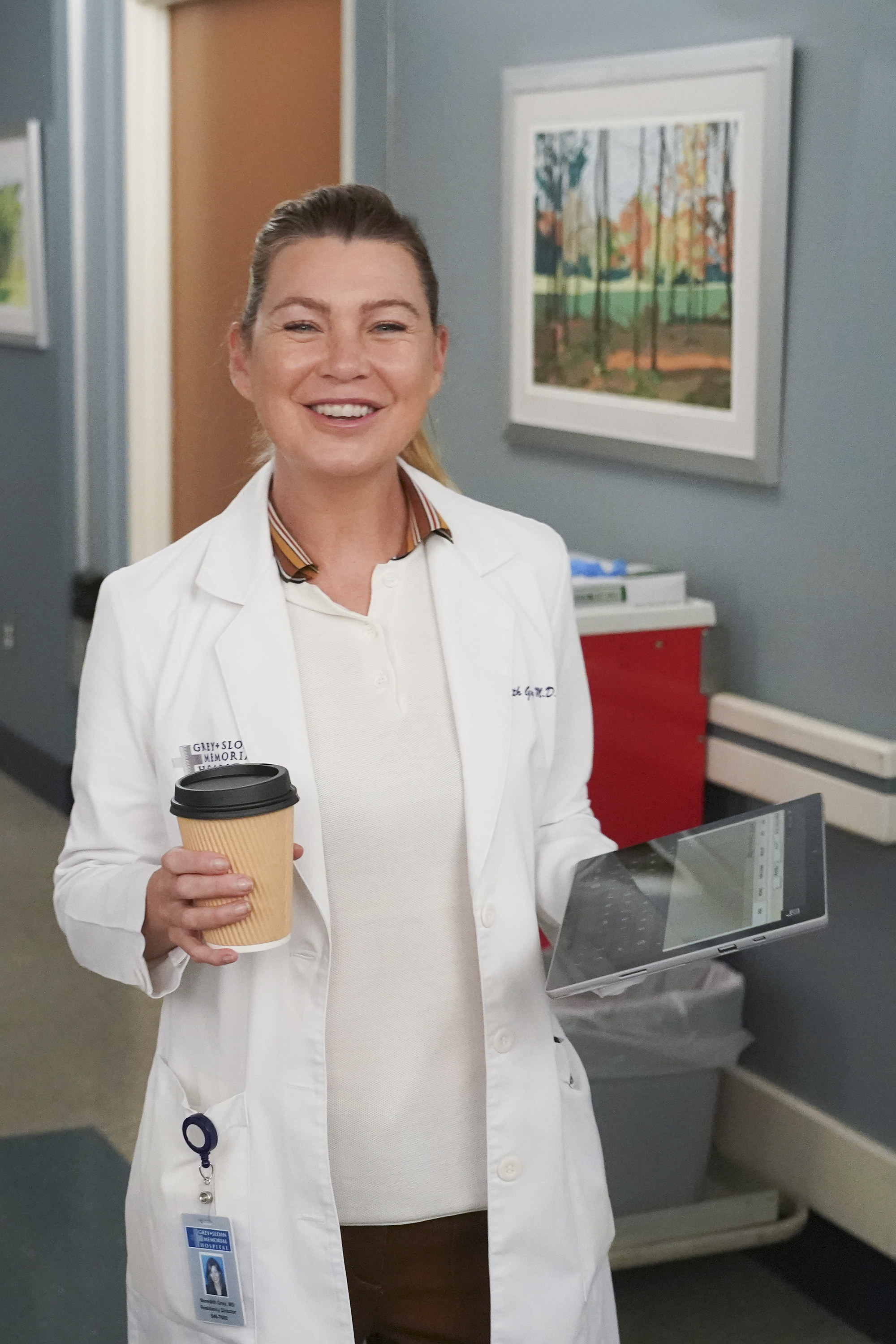 ellen in character in her doctor&#x27;s coat holding a tablet and a coffee