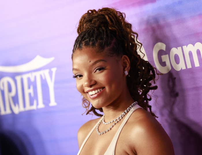 A close up photo of Halle Bailey smiling wearing a diamond necklace