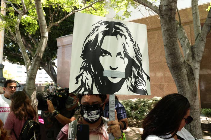 People holding signs, including with a drawing of Britney with her mouth covered with tape