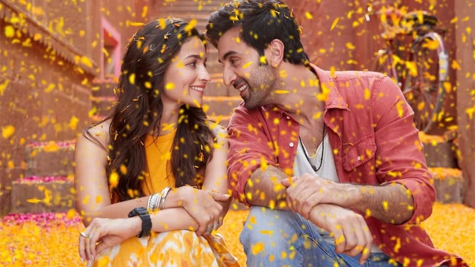Alia Bhatt and Ranbir Kapoor smiling at each other while flower petals fall on them