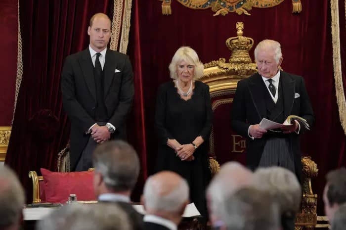 The three all stand in formalwear in front of an audience in a red velvet and gold gilded room