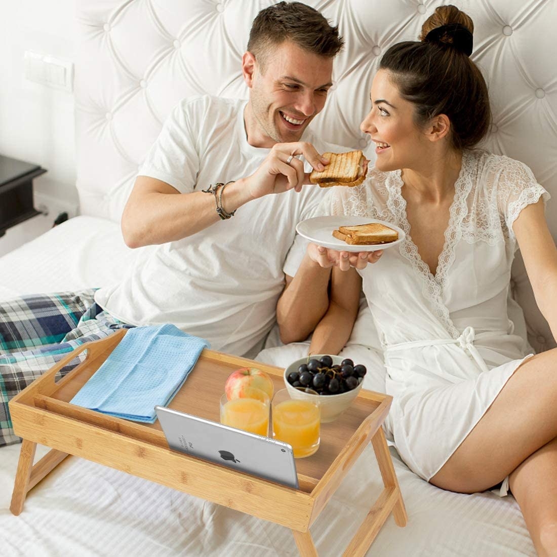 Two people in bed enjoying breakfast in bed with the tray table, which is also displaying ipad