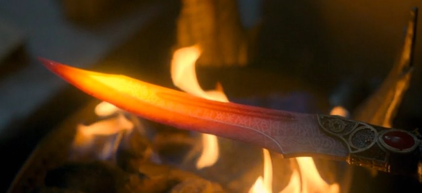 The catspaw dagger is held to a flame, showing writing inscribed on it