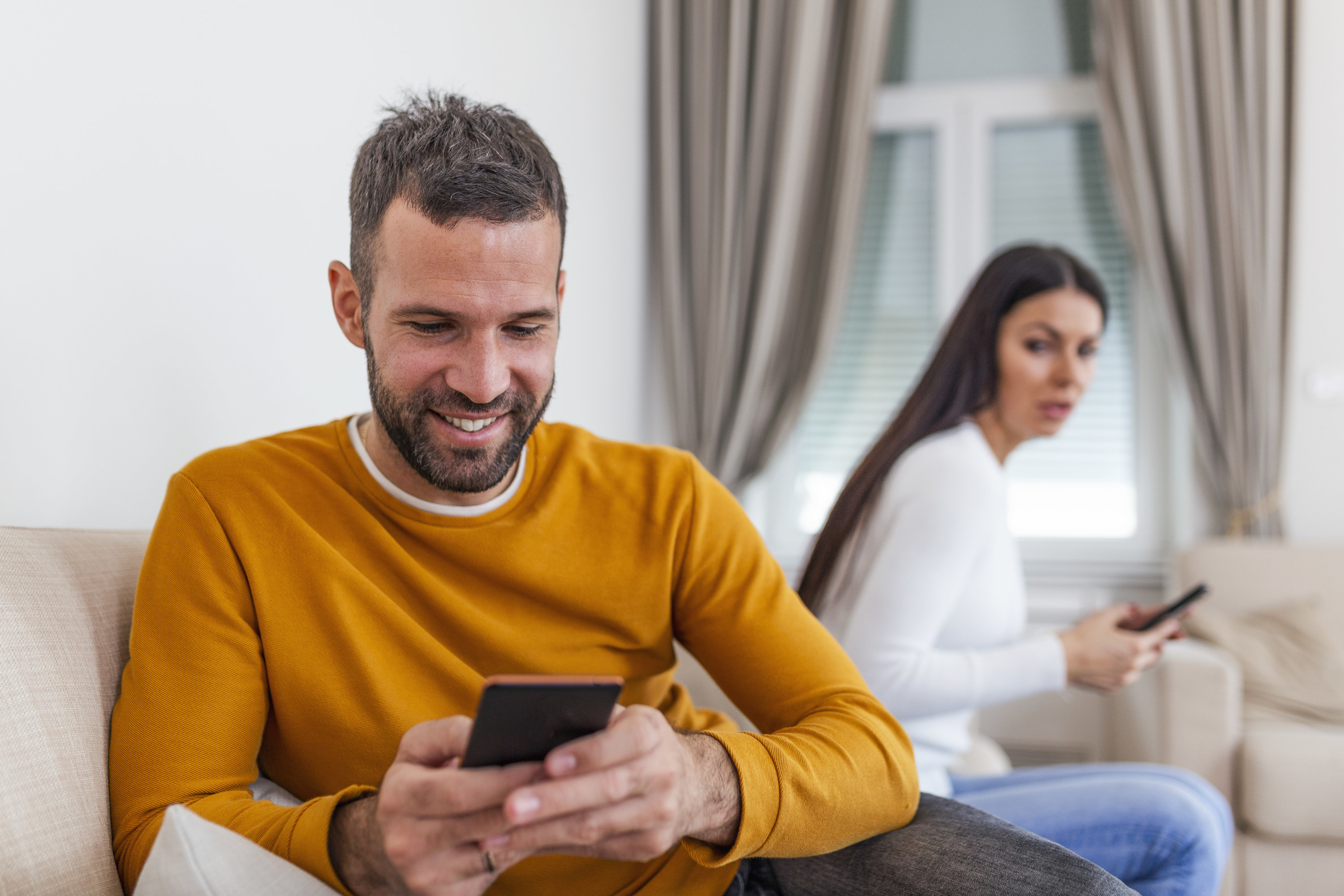 A man on his phone with his wife in the background