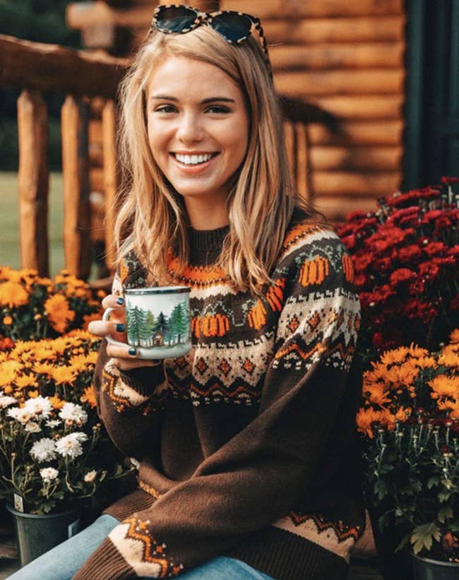 Model is wearing the brown fair isle sweater with pumpkins around the collar