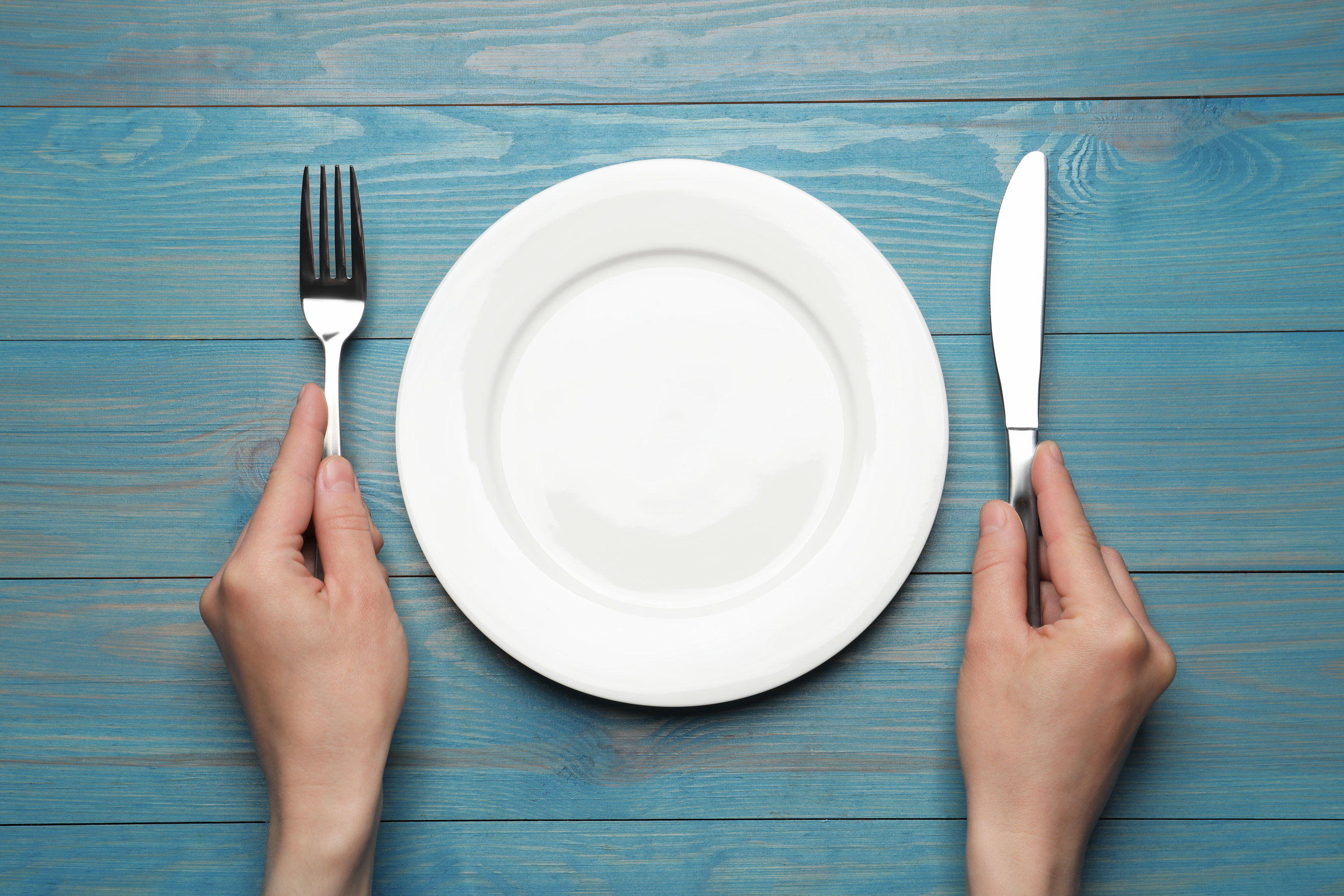 a person holding a knife and fork next to an empty plate