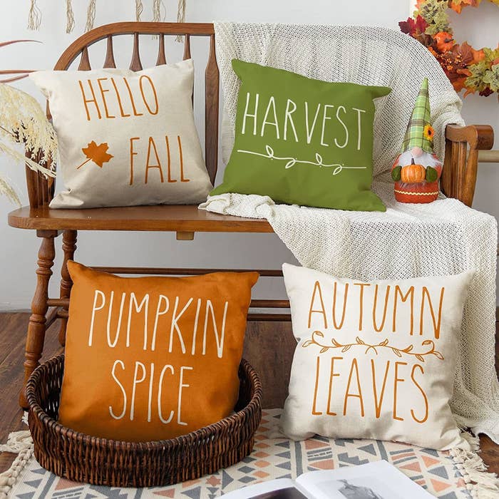 a set of four fall-themed cushion covers arranged artistically on a wooden bench