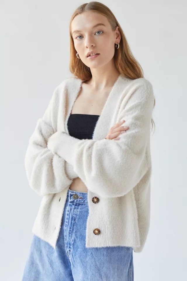 A person wearing the fuzzy cardigan with baggy jeans in front of a plain background