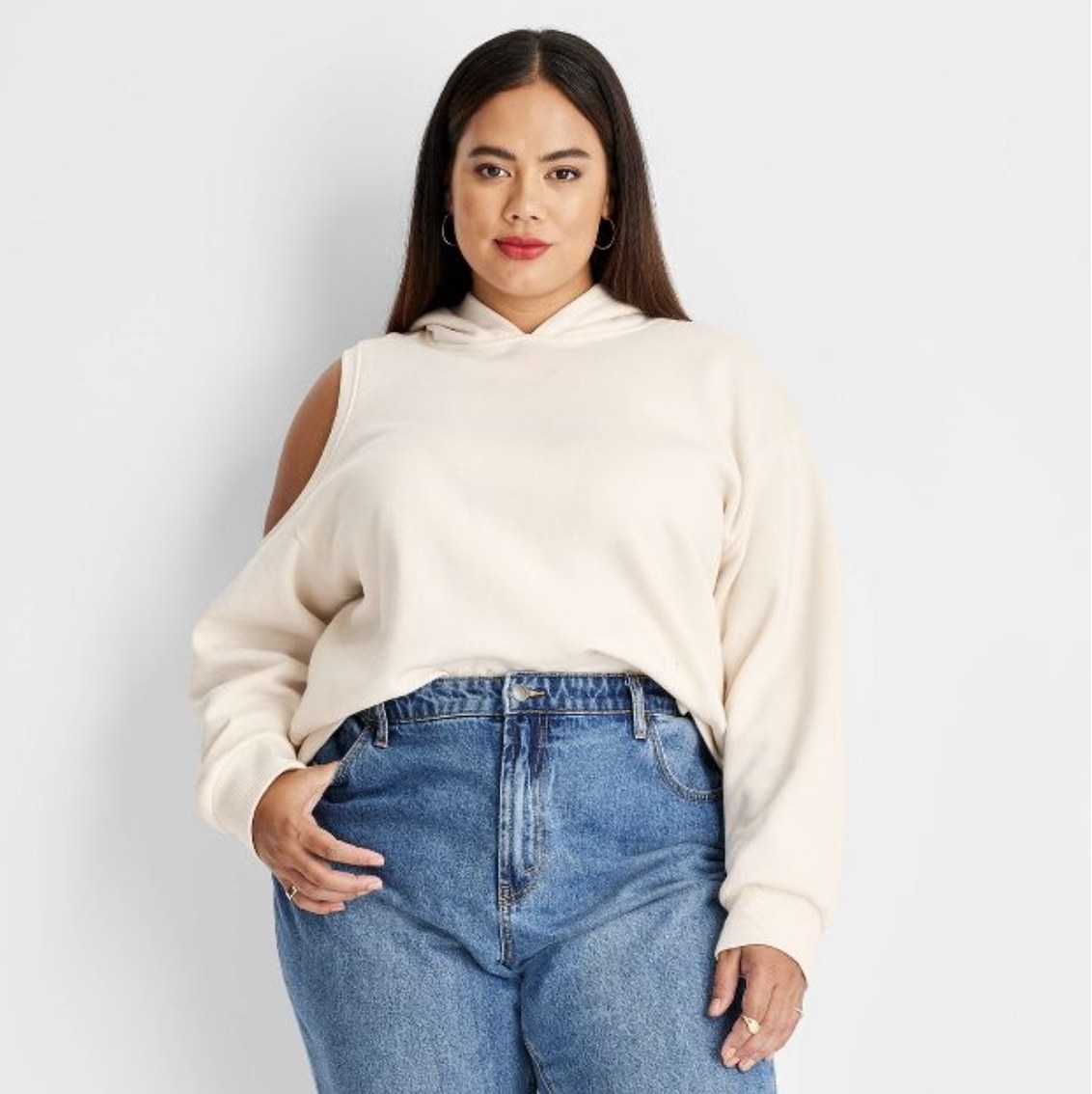 The model is wearing the cream sweater with shoulder cutouts and high waisted jeans