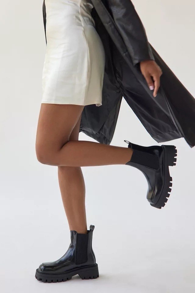 A person wearing the boots with a dress and jacket in front of a plain background