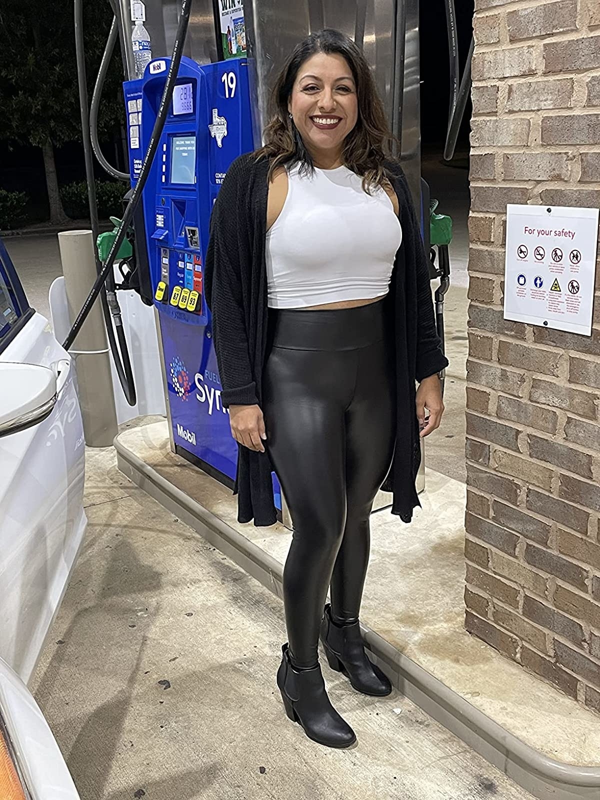 Reviewer wearing black faux leather leggings, boots, white crop top and black cardigan