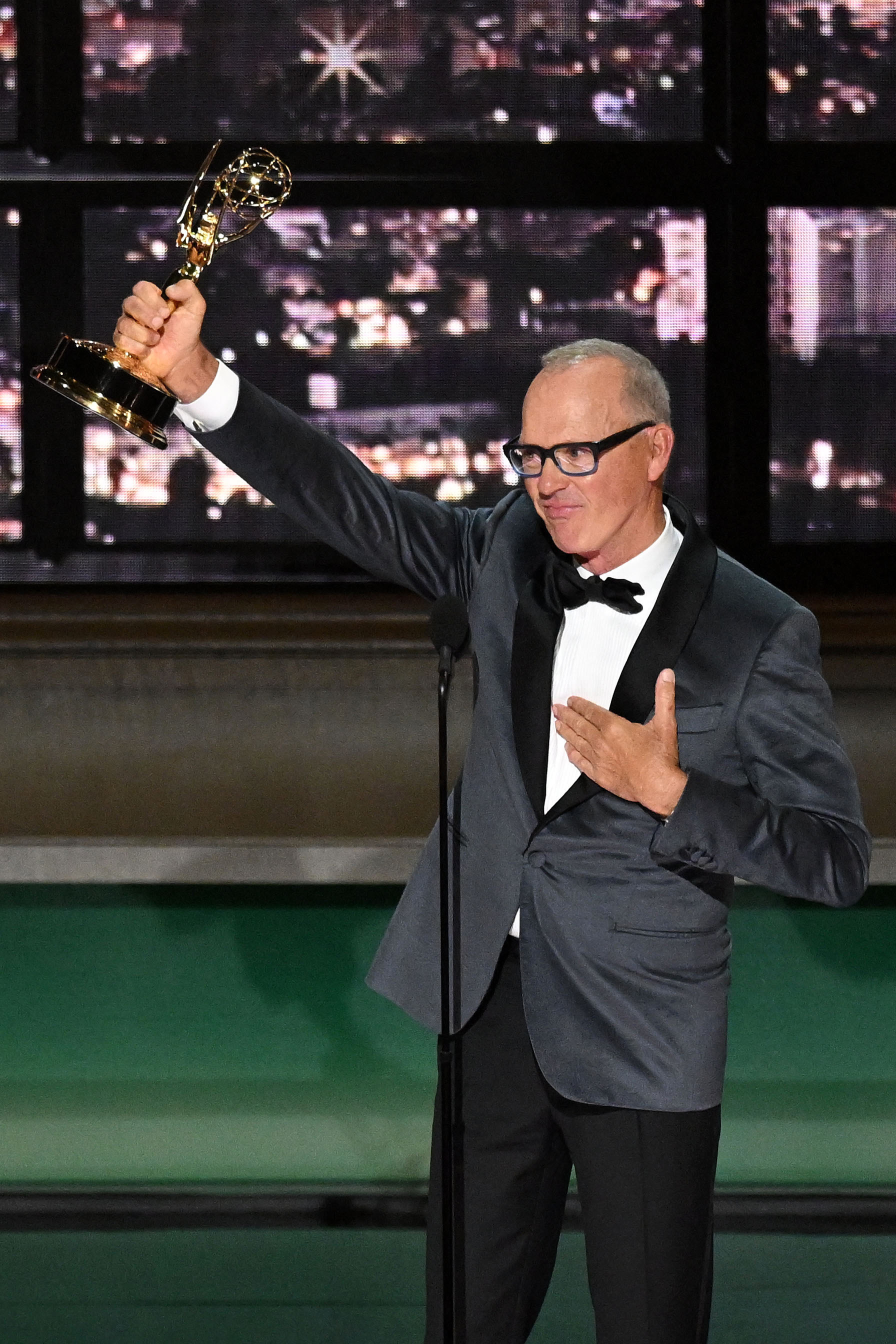 Michael Keaton holding his Emmy up in the air