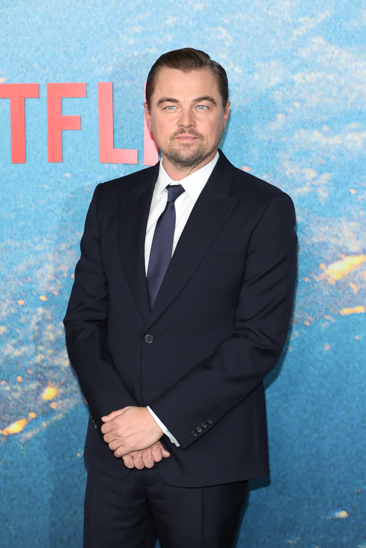 Leonardo DiCaprio standing by a blue backdrop
