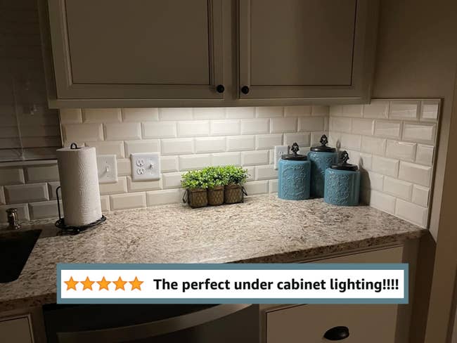 A kitchen counter illuminated with under cabinet lighting, caption 