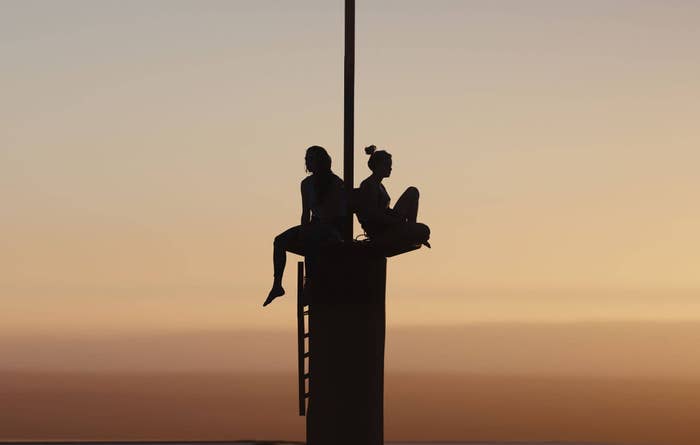 Two women sit atop a large pole