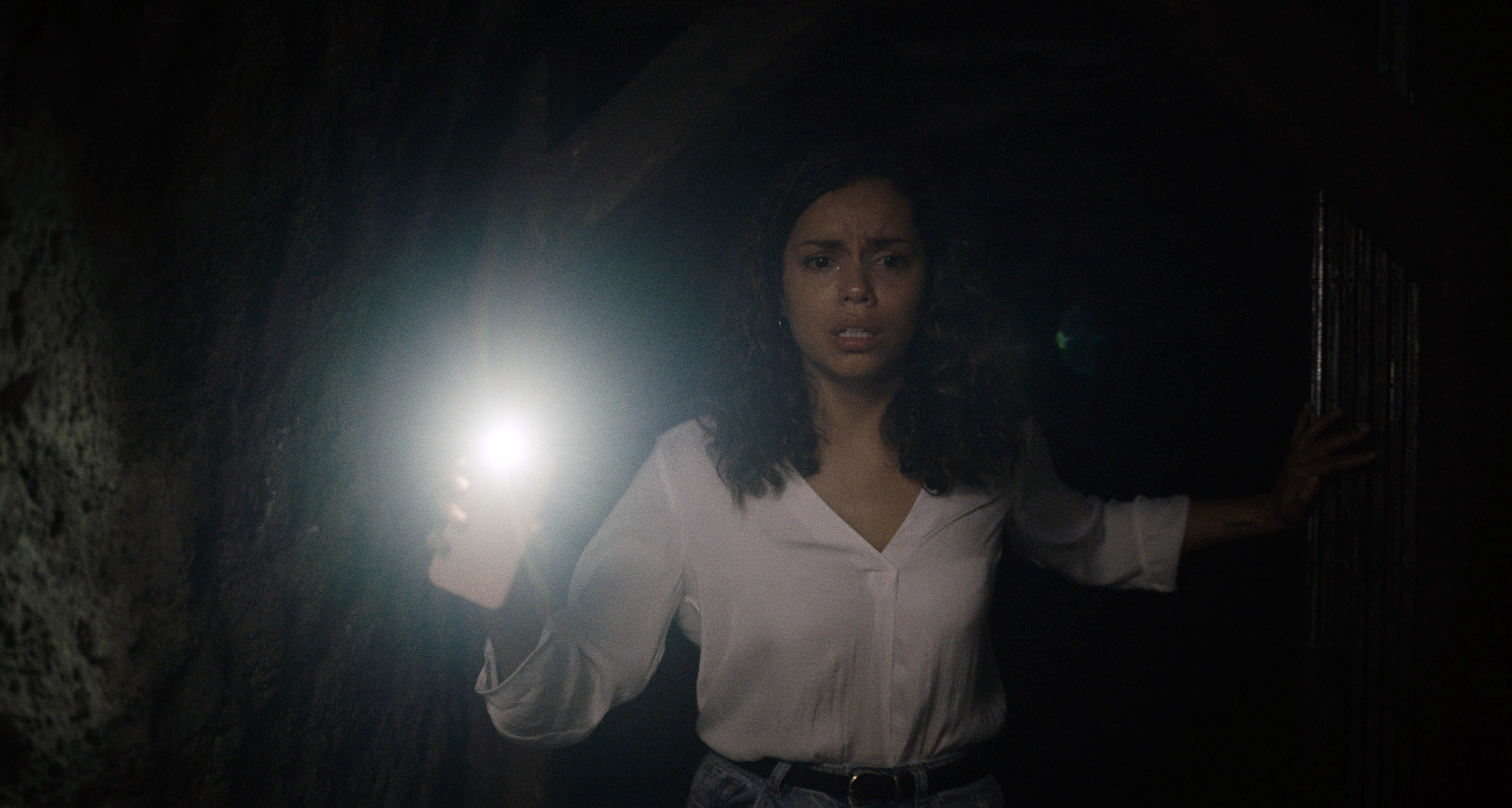 A woman walks through a dark tunnel using her phone flashlight for light