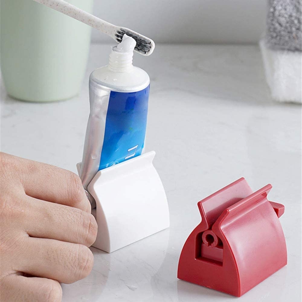 The toothpaste squeezers in red and white. The white toothpaste squeezer is holding a tube of toothpaste, while a model uses it to squeeze toothpaste onto their toothbrush.