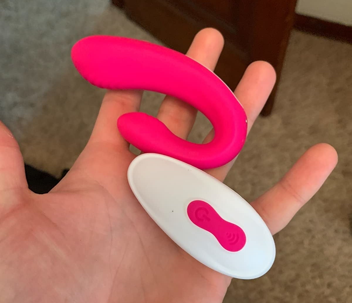 Reviewer holding pink g-spot vibrator and white wireless remote