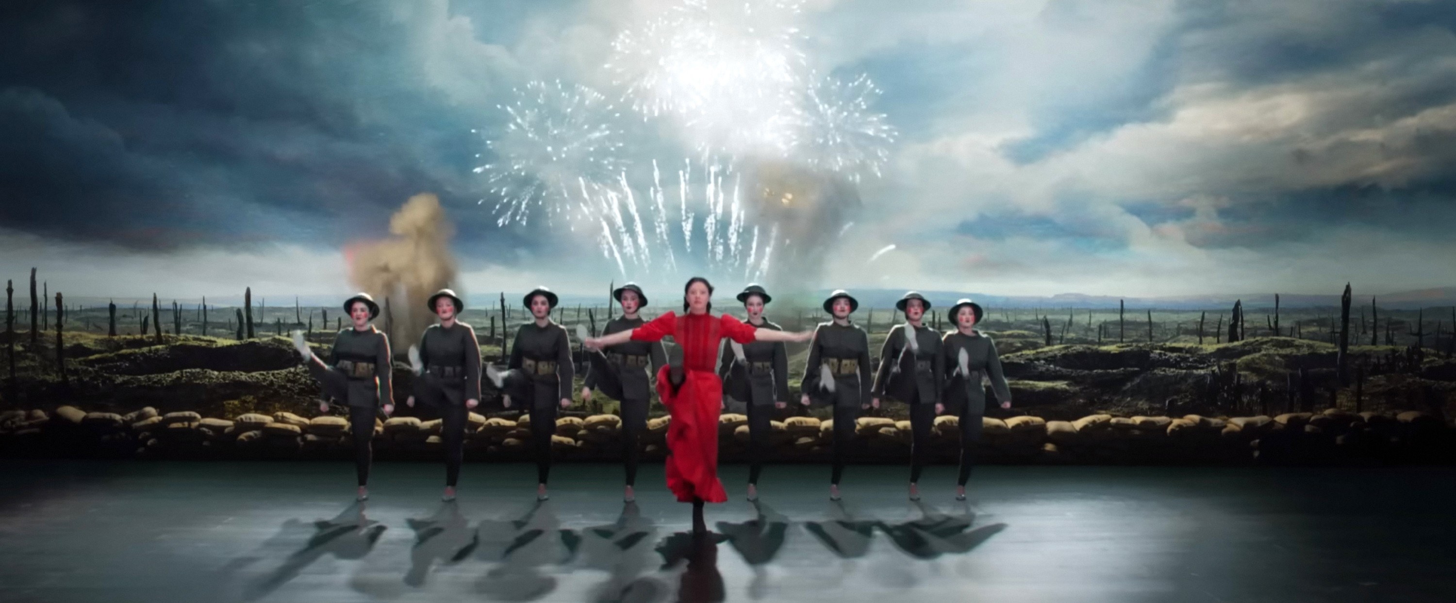 A woman in a bright red dress joins a kick line of women dressed as soldiers