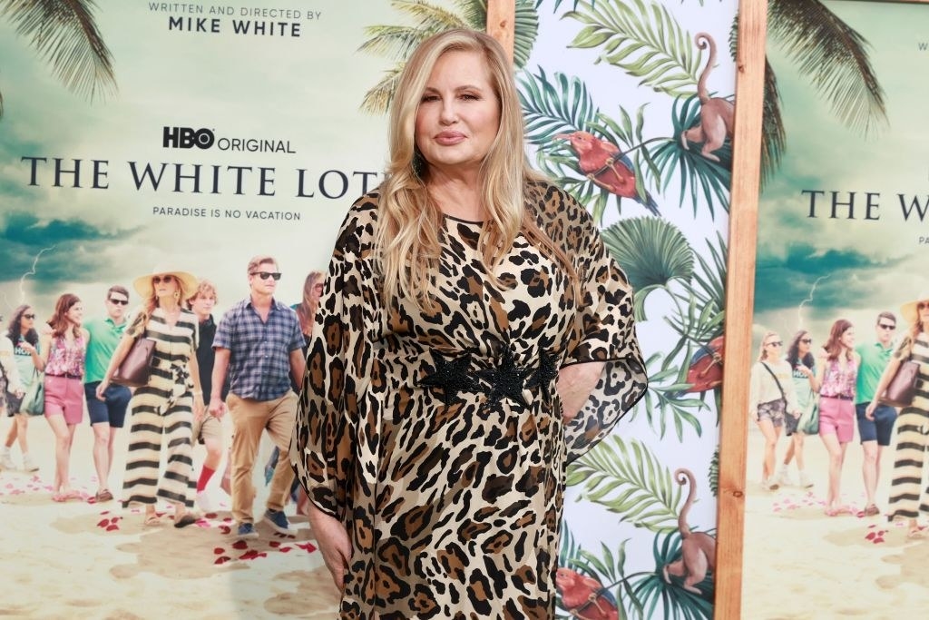 Jennifer in an animal-print dress in front of The White Lotus poster