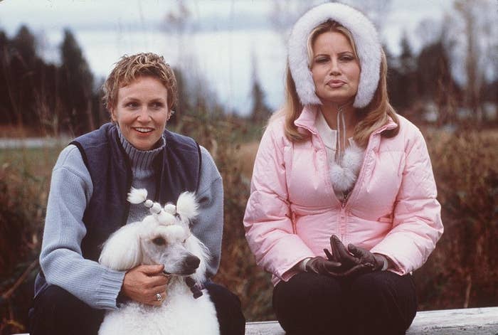 Jennifer wearing a puffy short pink jacket and sitting next to Jane Lynch, who&#x27;s holding a poodle