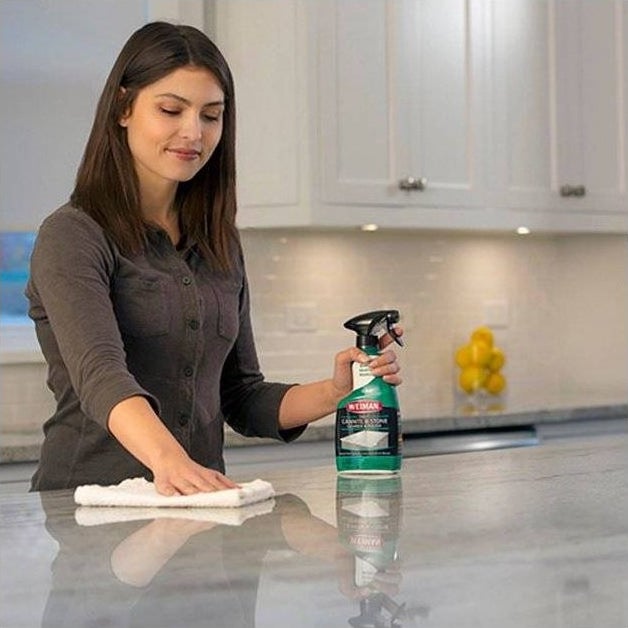 a model using the green and black bottle of cleaner on a white stone countertop