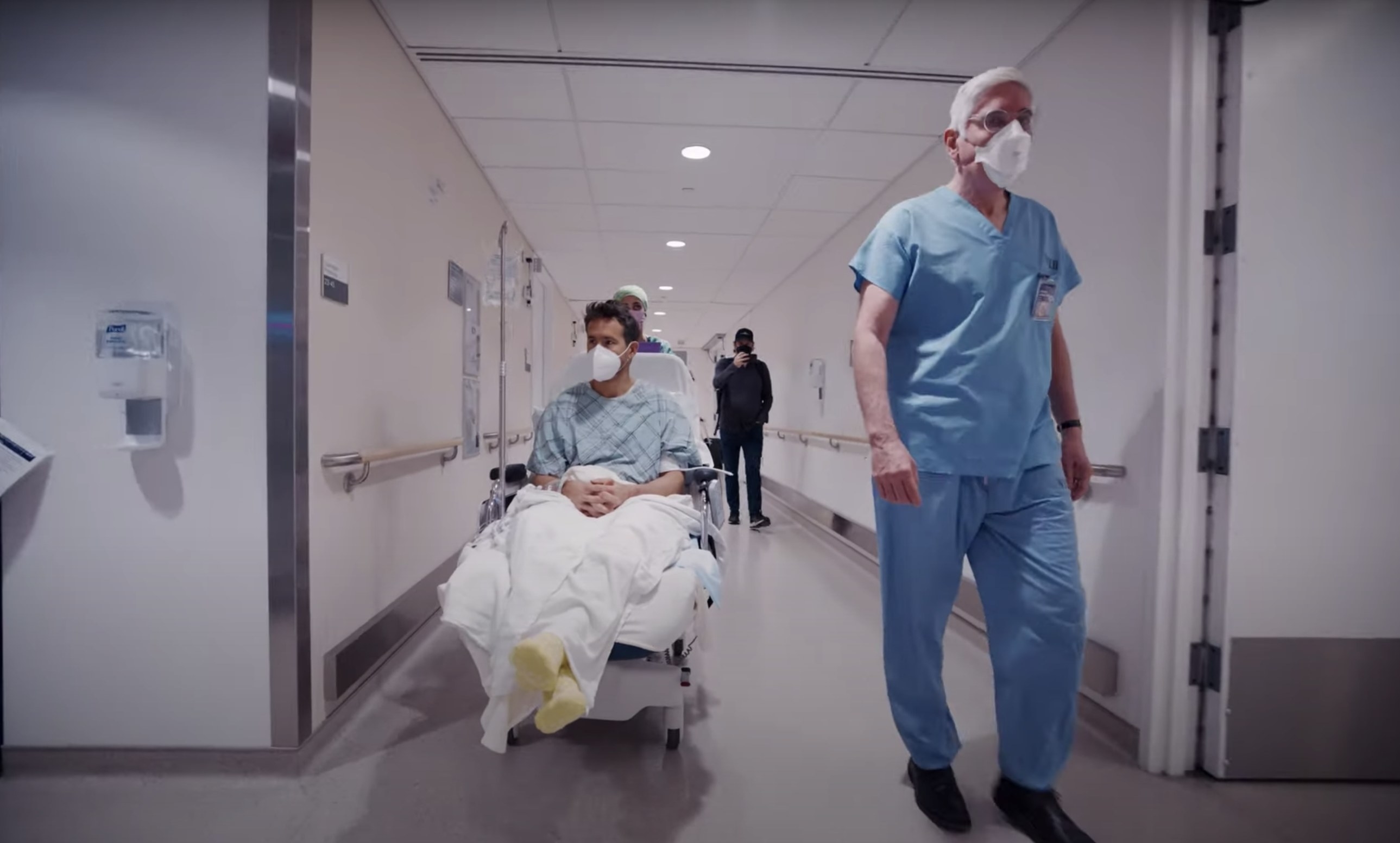 A doctor walks next to Ryan as he is wheeled through a hospital