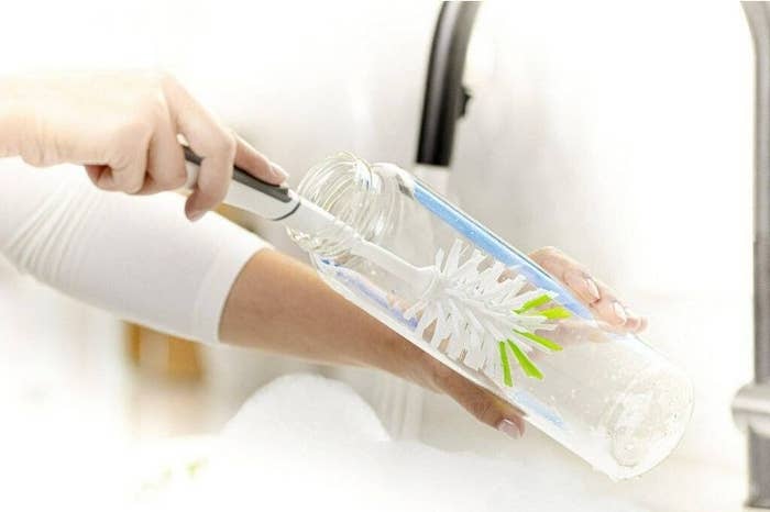 a photo of a model using the white and green brush to clean the bottom of a glass bottle