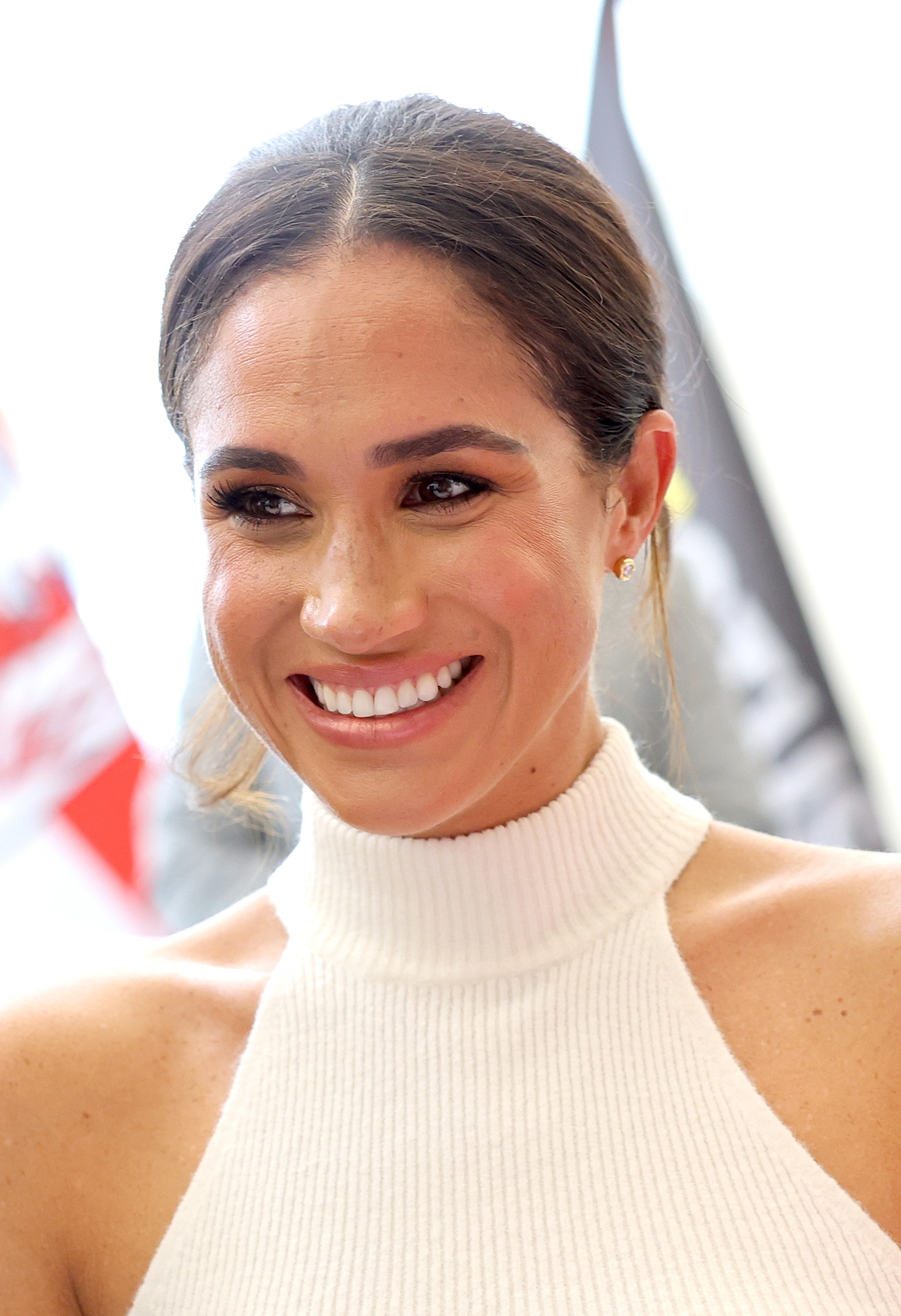 Head and shoulders image of Meghan in a white knitted high neck vest, smiling at the camera with her hair tied back