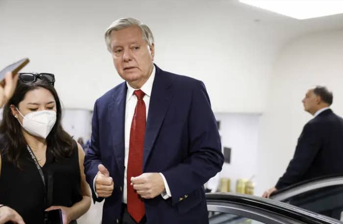 Lindsey Graham stands in a navy suit and red tie next to a masked woman