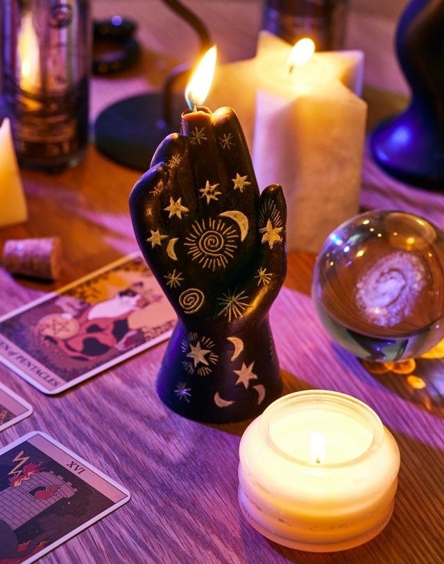a hand shaped candle on a table surrounded by tarot cards