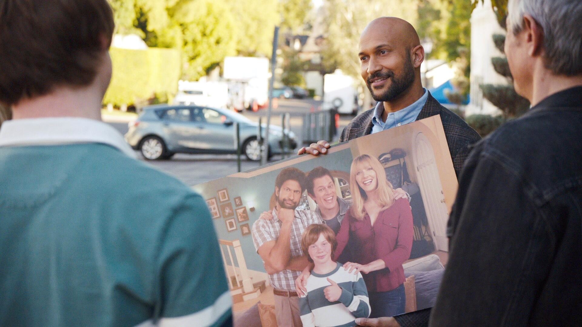 a man holding up a poster of a TV family to the actors