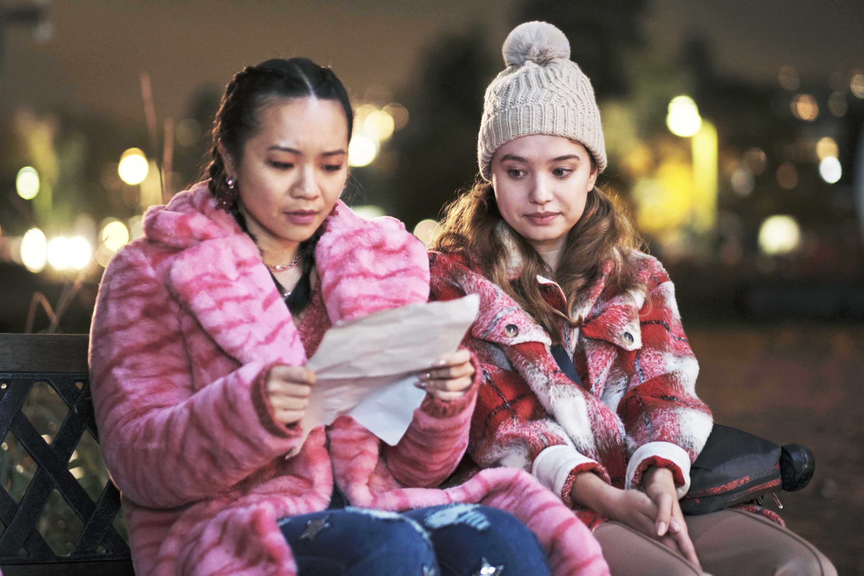 two girls sitting outside in winter clothing and looking at a piece of paper
