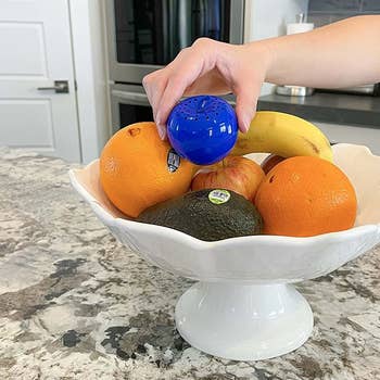 a model placing the apple-shaped produce saver into a bowl of fruit