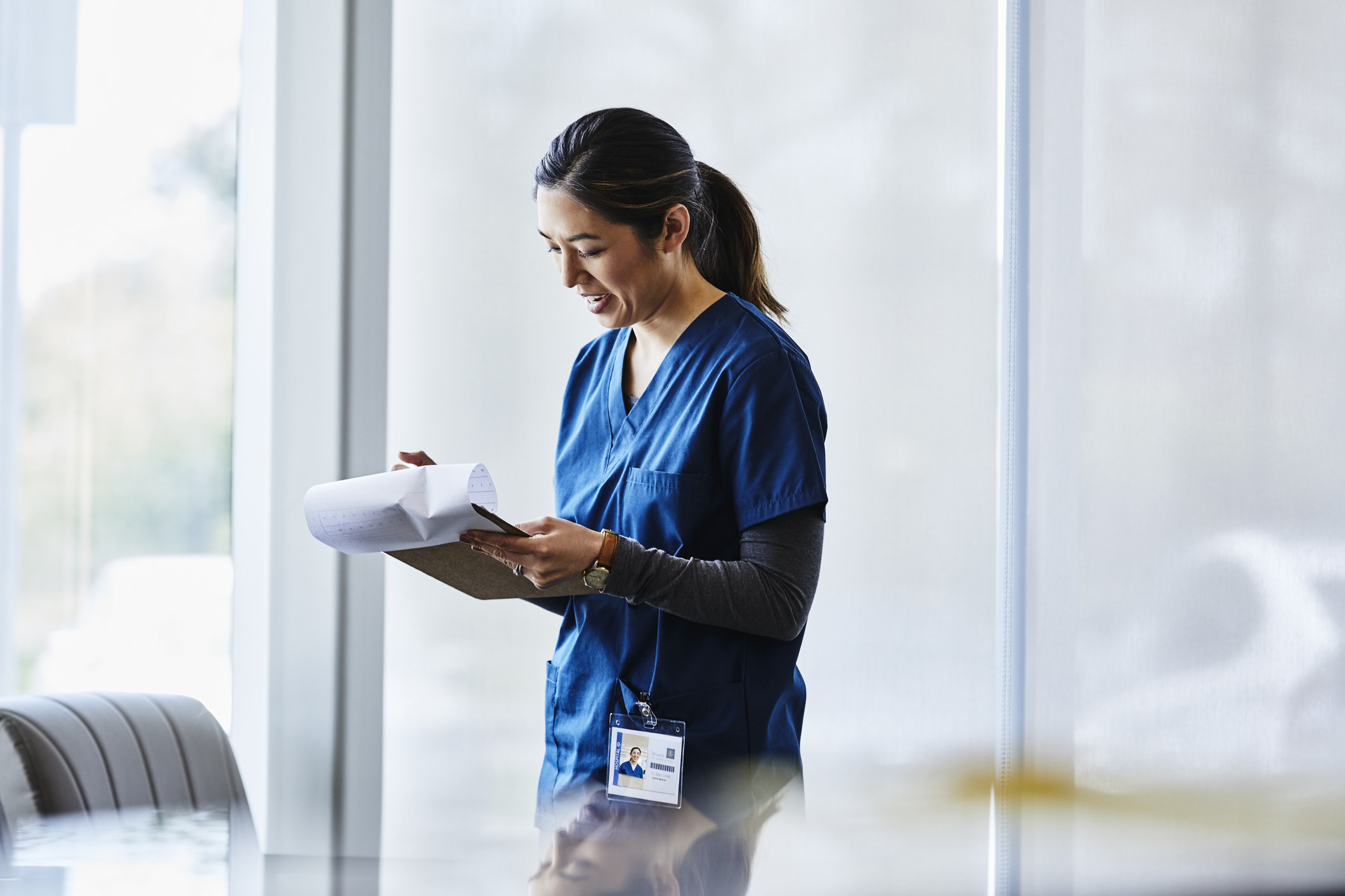 woman in scrubs making notes on a clipboard