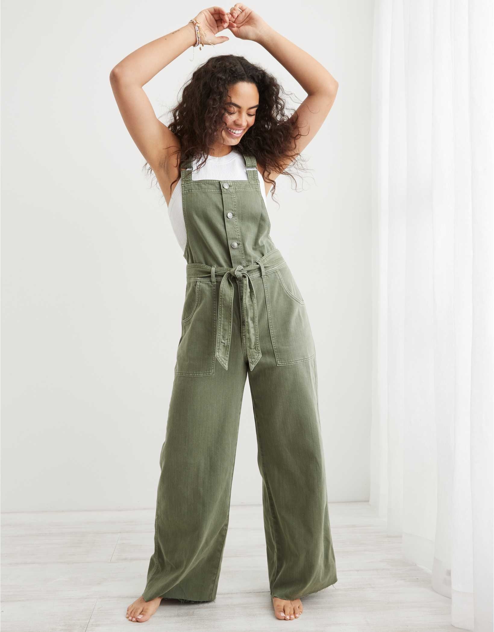 model in sage green linen-y overalls with a buttoned front and waist tie