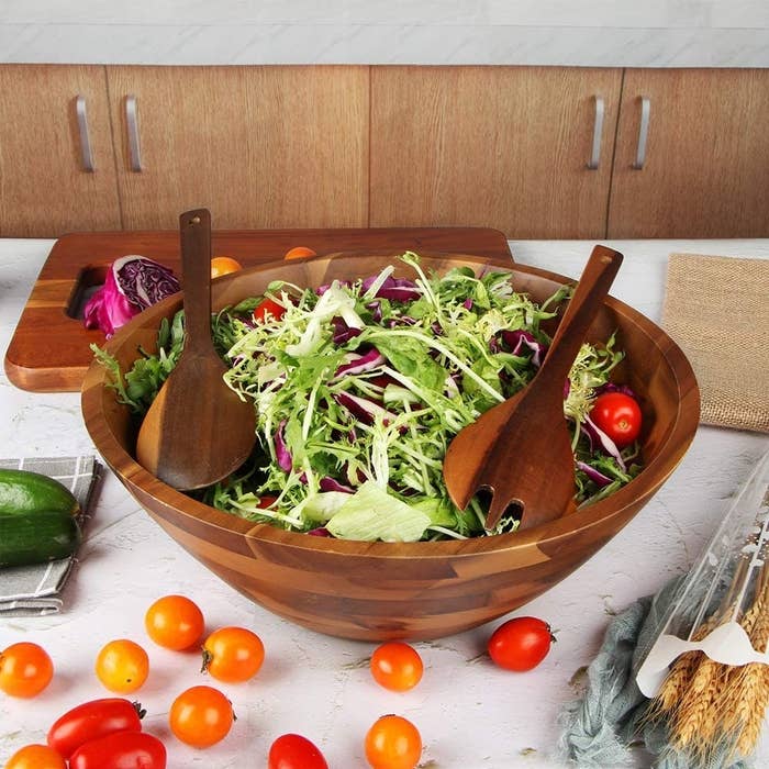 the salad bowl with some spring mix in it and serving tools on top