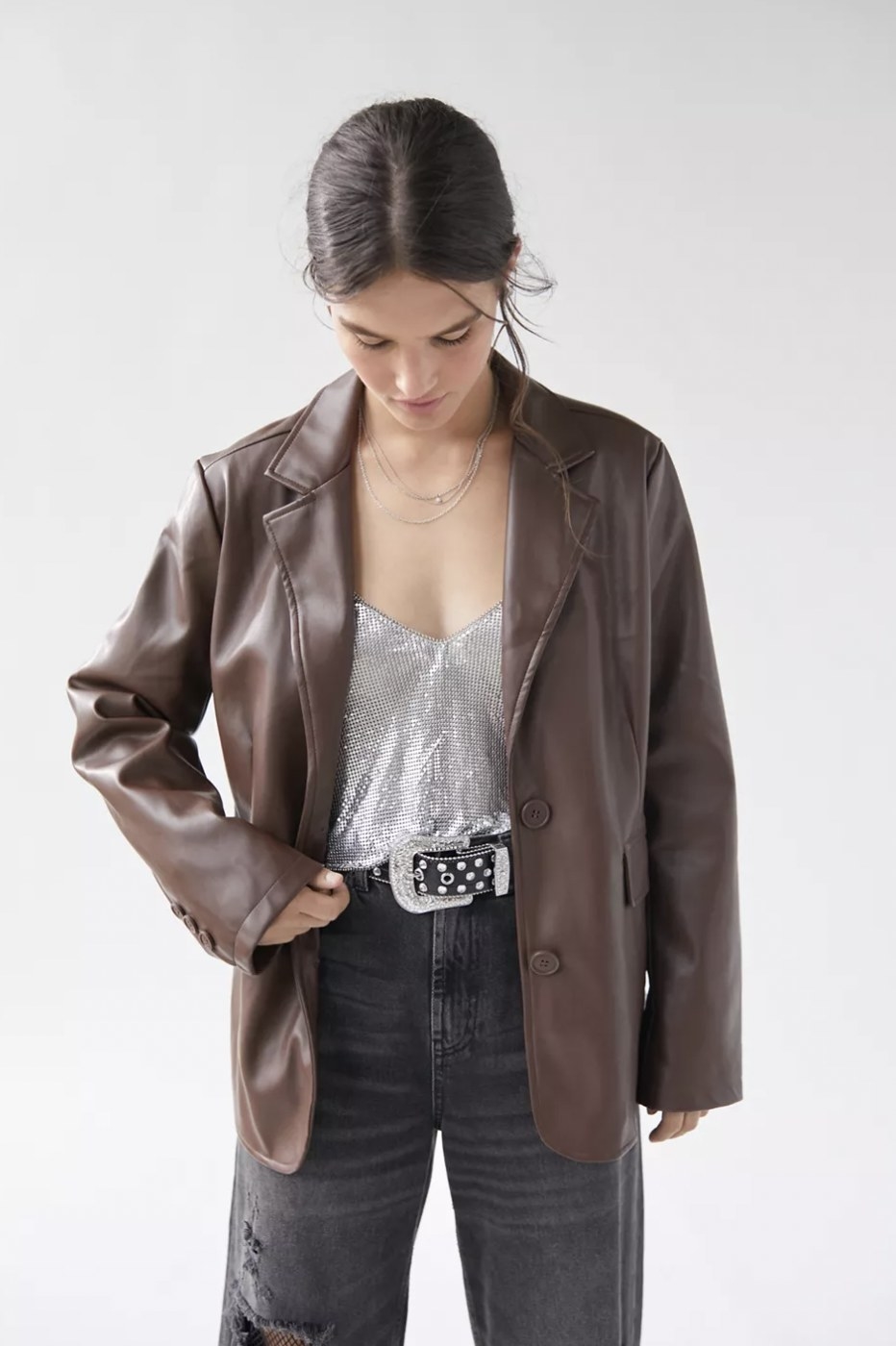 Model looking down while wearing the brown jacket over sparkly tank and black jeans
