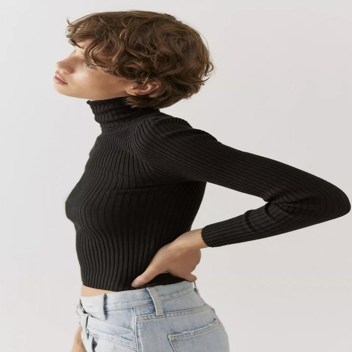Model from side looking off in the distance in black cropped turtleneck sweater