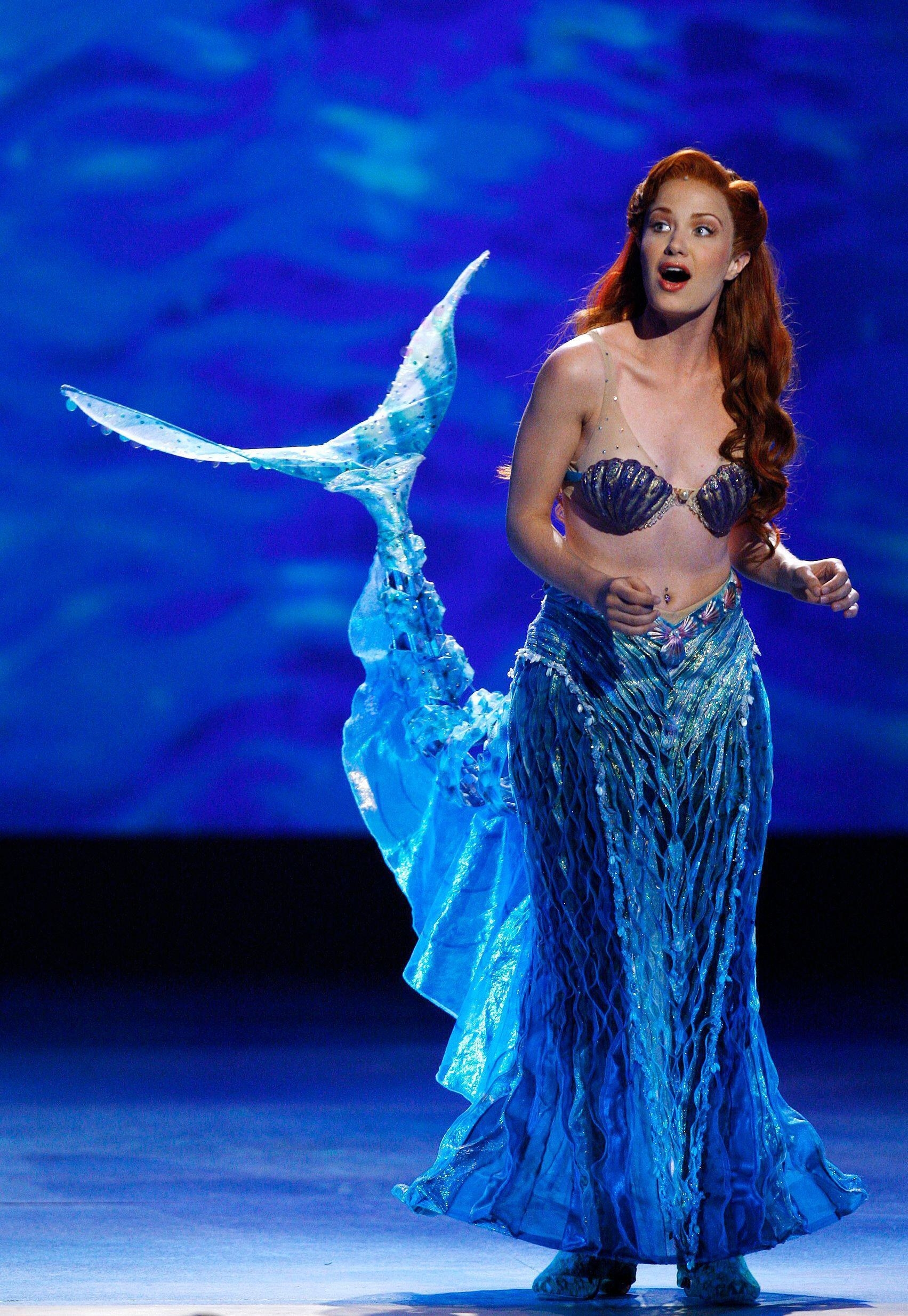 Sierra singing on stage with a large mermaid tail behind her