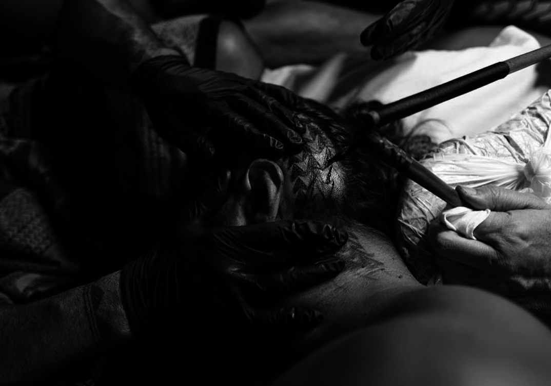 Two gloved hands hold Jason&#x27;s head down as someone else taps the ink into the tattoo