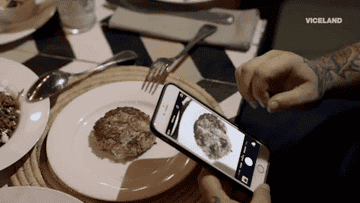 person trying to take an iphone photo of their meal at a dimly-lit restaurant