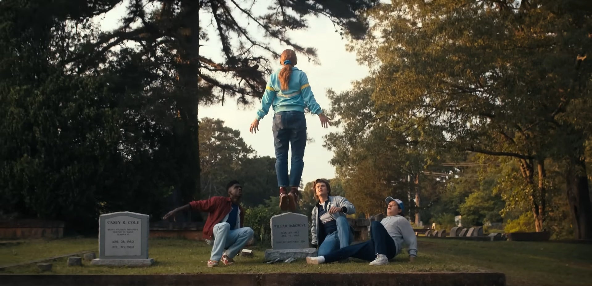 a girl levitating by a tombstone as other teenagers look up at her, astonished