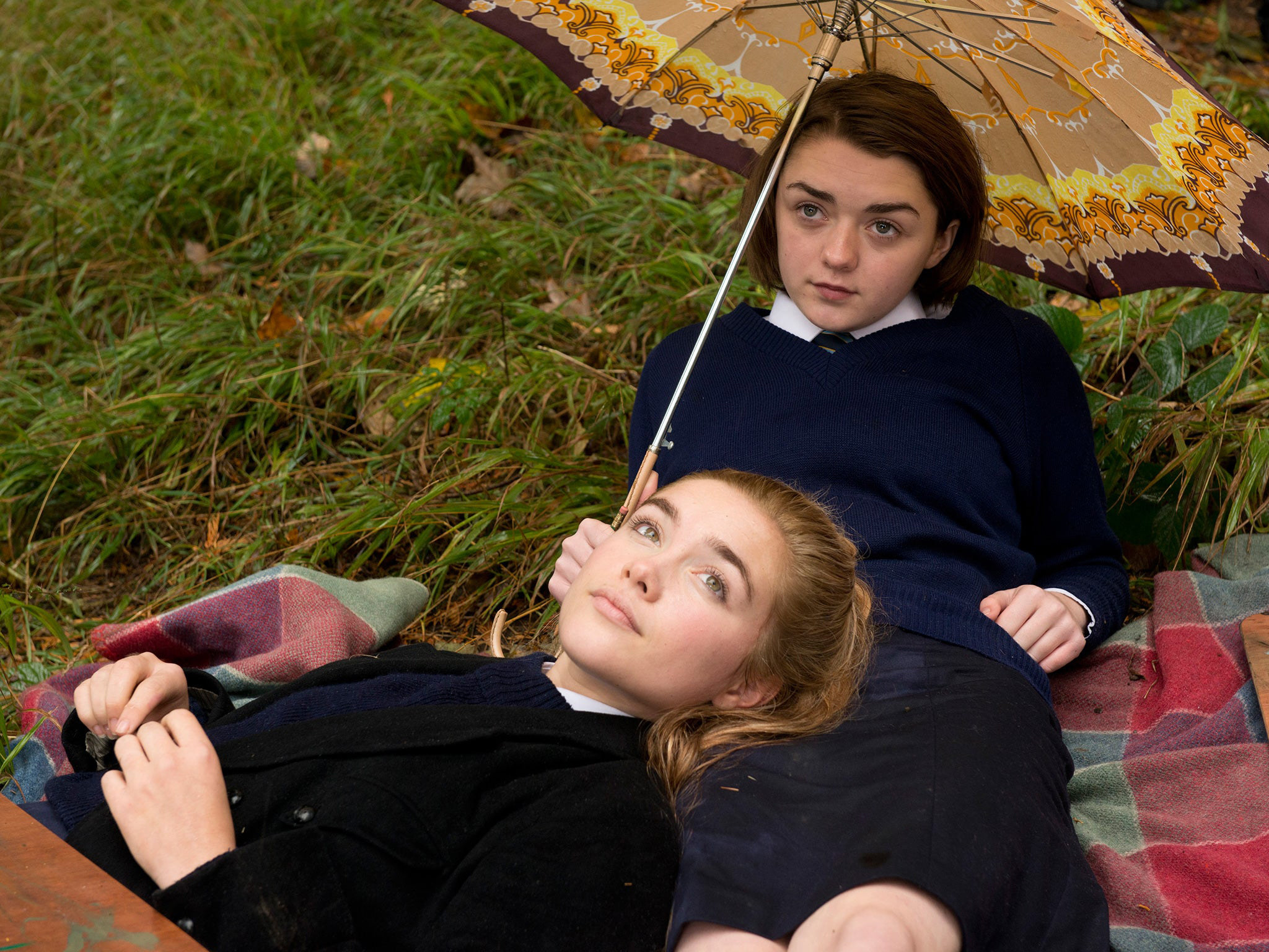 Florence Pugh lays on the lap of Maisie Williams on the grass
