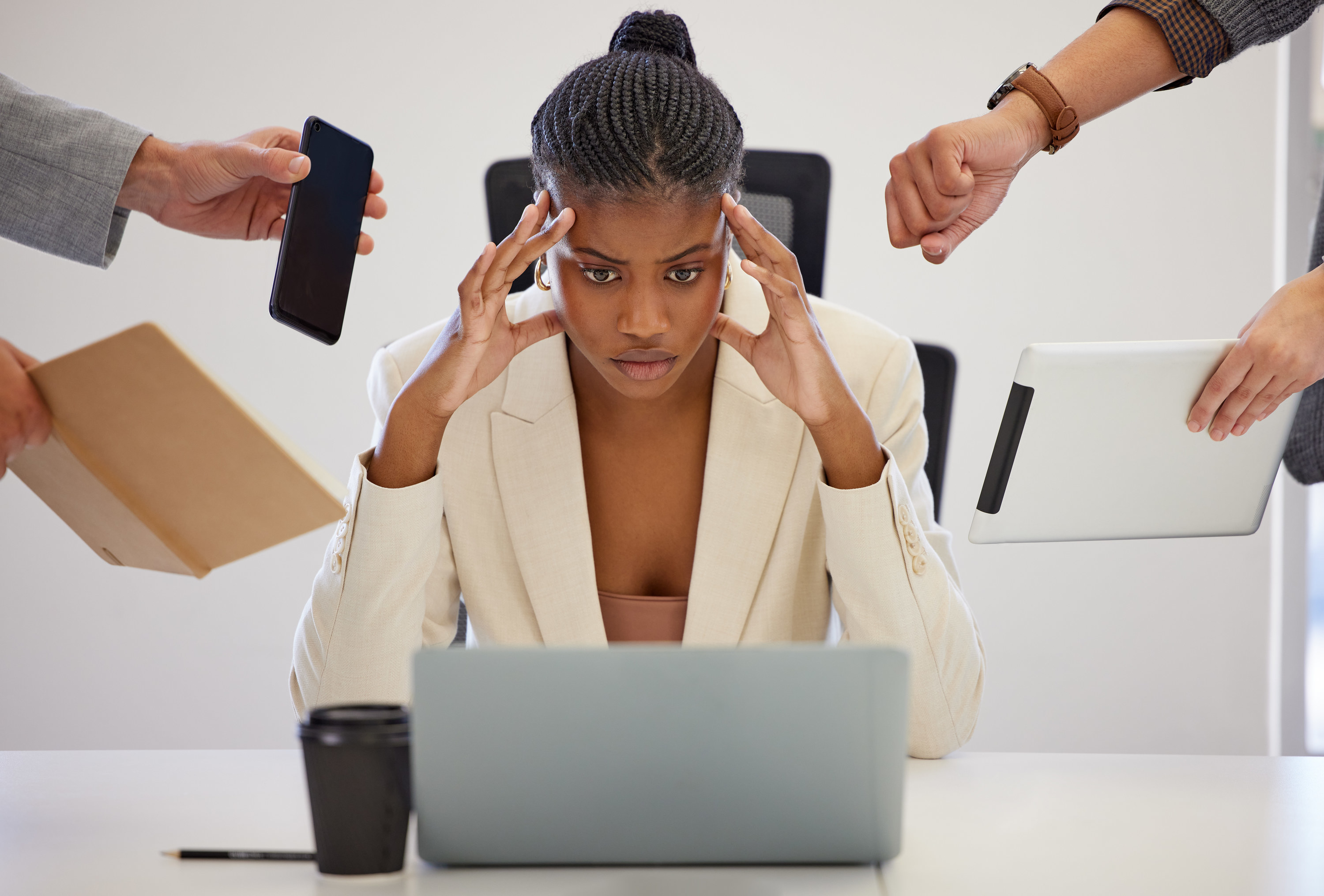 stressed woman sitting at a desk as people hand her work items from all directions